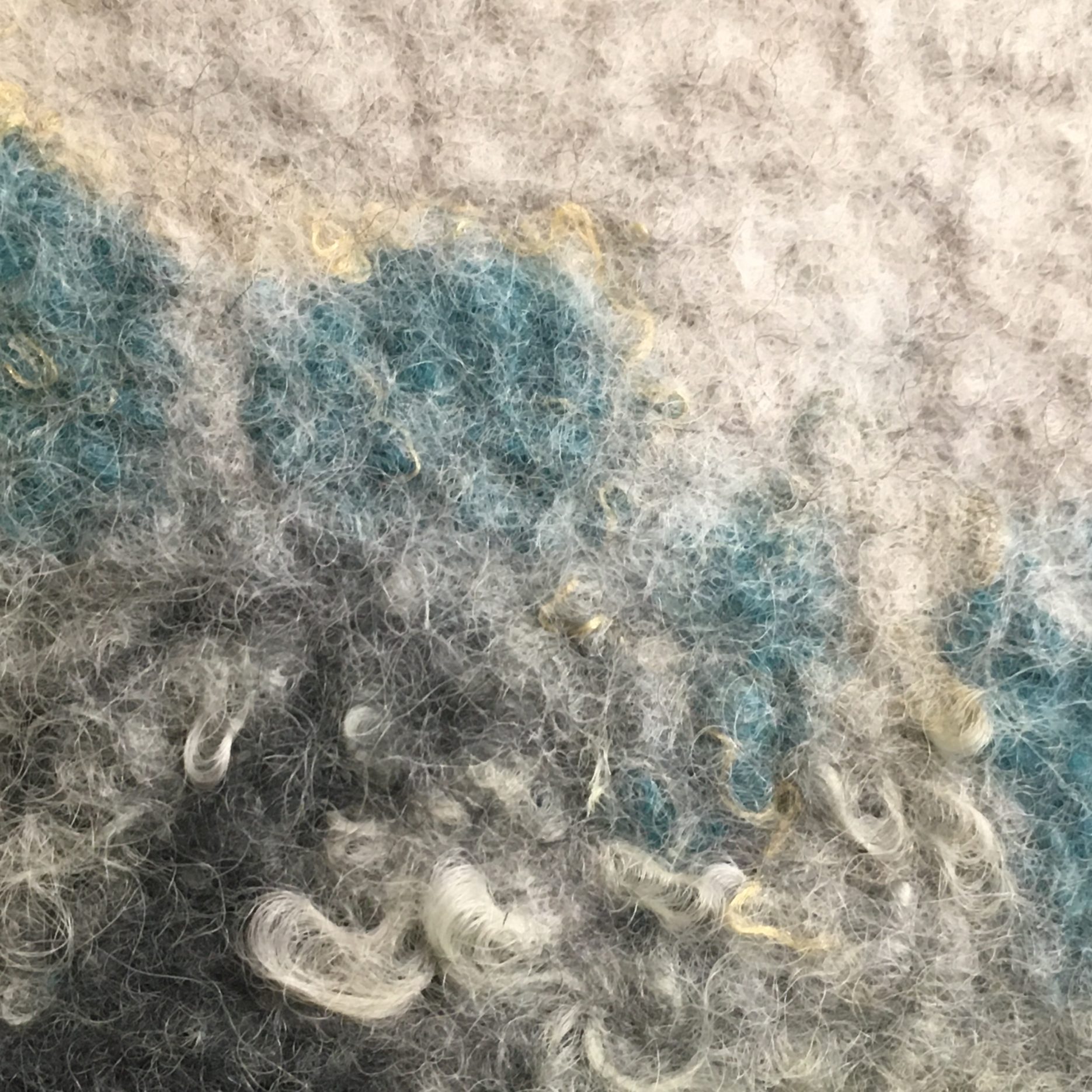 Detail of wet felted bag, showing gradation from dark to light gray, lower left to upper right, with teal, gold and silver accents