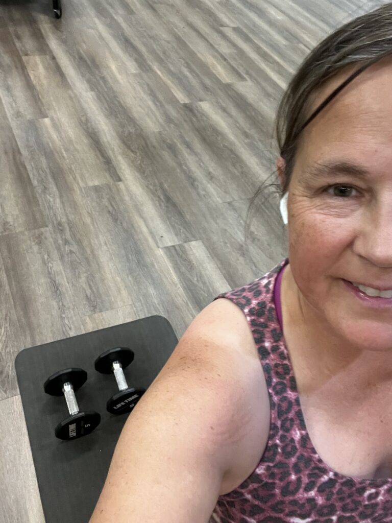 Selfie showing half my face, shoulder, and looking down at a yoga mat and dumbbells.
